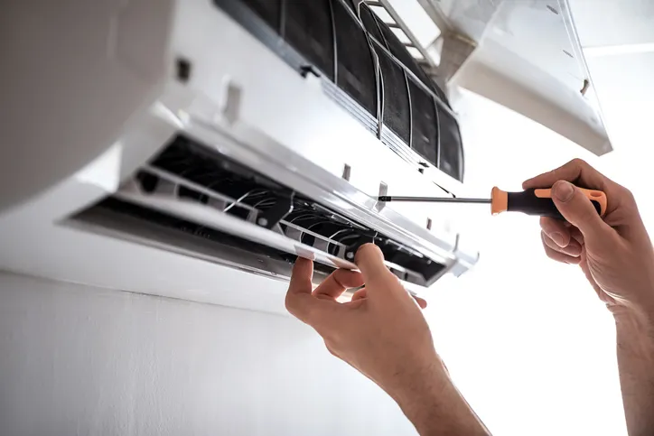A person skillfully uses a screwdriver to repair an air conditioning unit mounted on the wall, showcasing expert AC repair in Woburn, MA.
