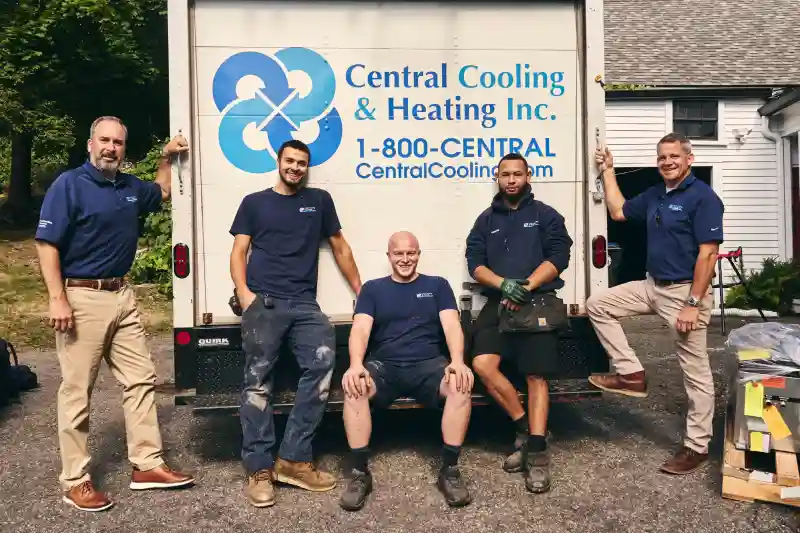 Five men in branded shirts and trousers stand and sit in front of a Central Cooling & Heating Inc. truck parked on a driveway.